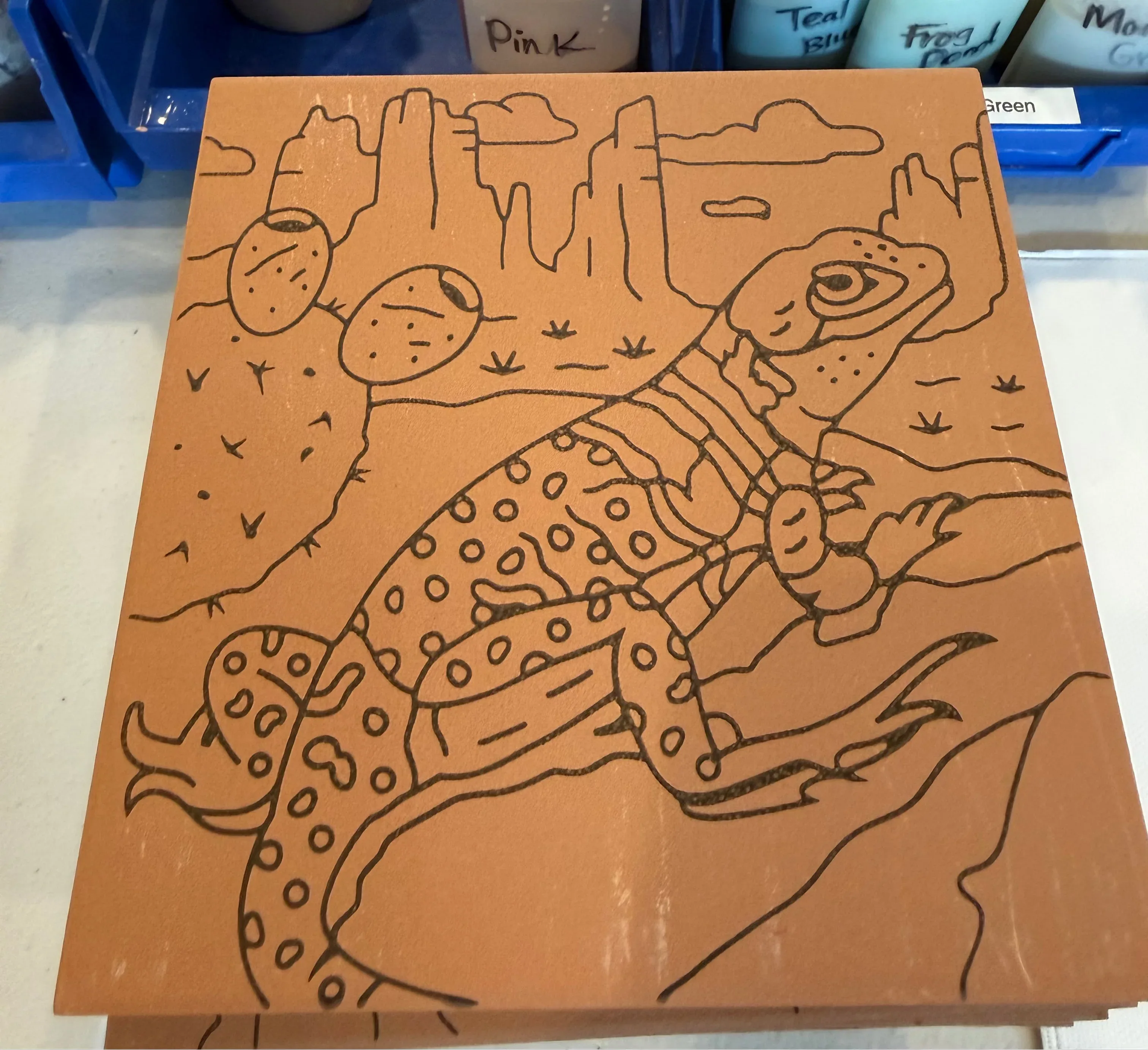 Wooden board with a lizard design on a table with art supplies in the background