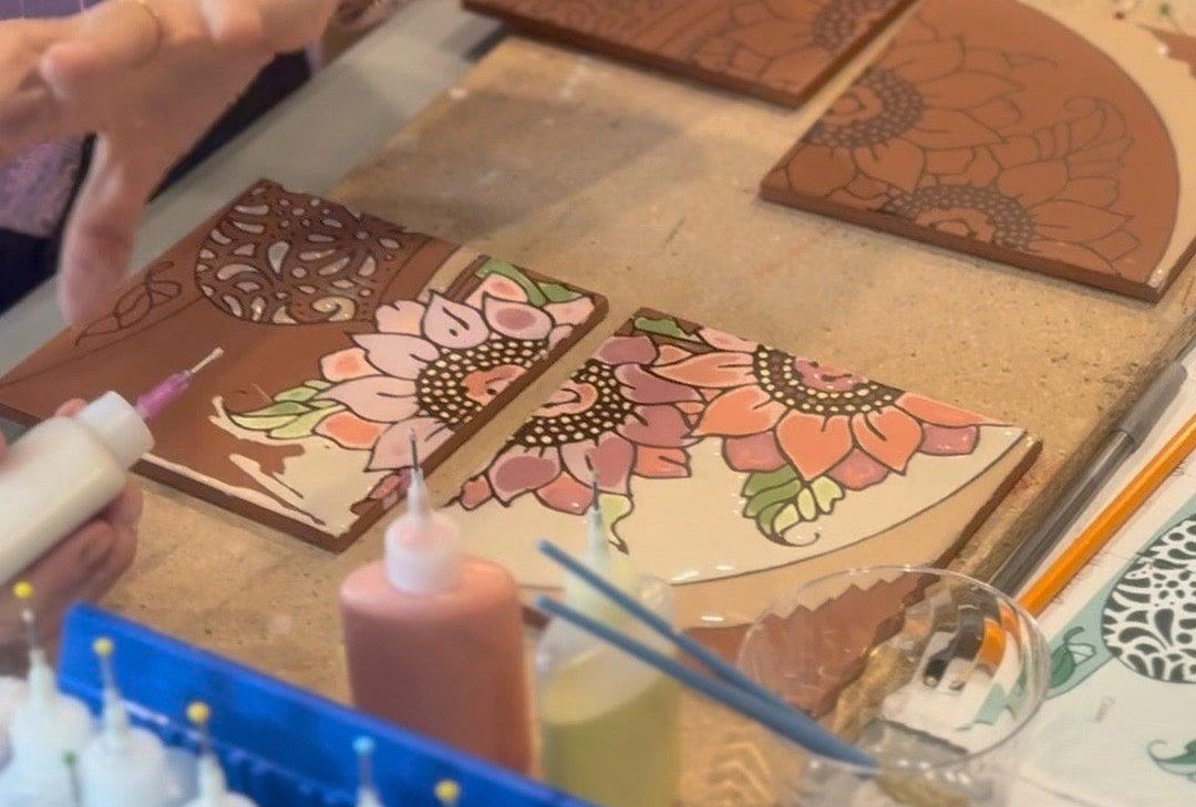 Person working on decorative items with a box of paint bottles in the foreground.